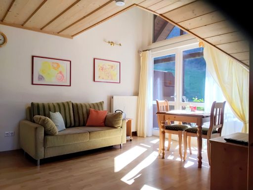 Helles Wohnzimmer mit grüner Couch, Esstisch und großen Fenstern.