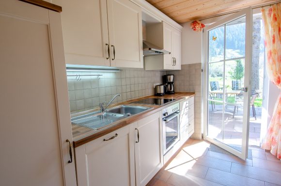 Helle Küche mit weißen Schränken, Kaffeemaschine und Zugang zur Terrasse.