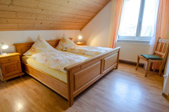 Gemütliches Zimmer mit Doppelbett, Holzinterieur und Fenster mit Vorhängen.